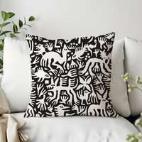 Primitive white hand-drawn animals and plant life. Printed on a black background. Pillow on a couch.