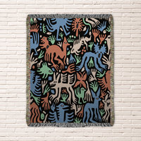 woven blanket with Modern folk art of otherworldly dinosaurs, flora and fauna in brown, beige, green and blue on a black background. 