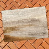 Neutral area rug with an abstract coastal haze design in taupe, beige, and soft grey tones on a brick patio floor.