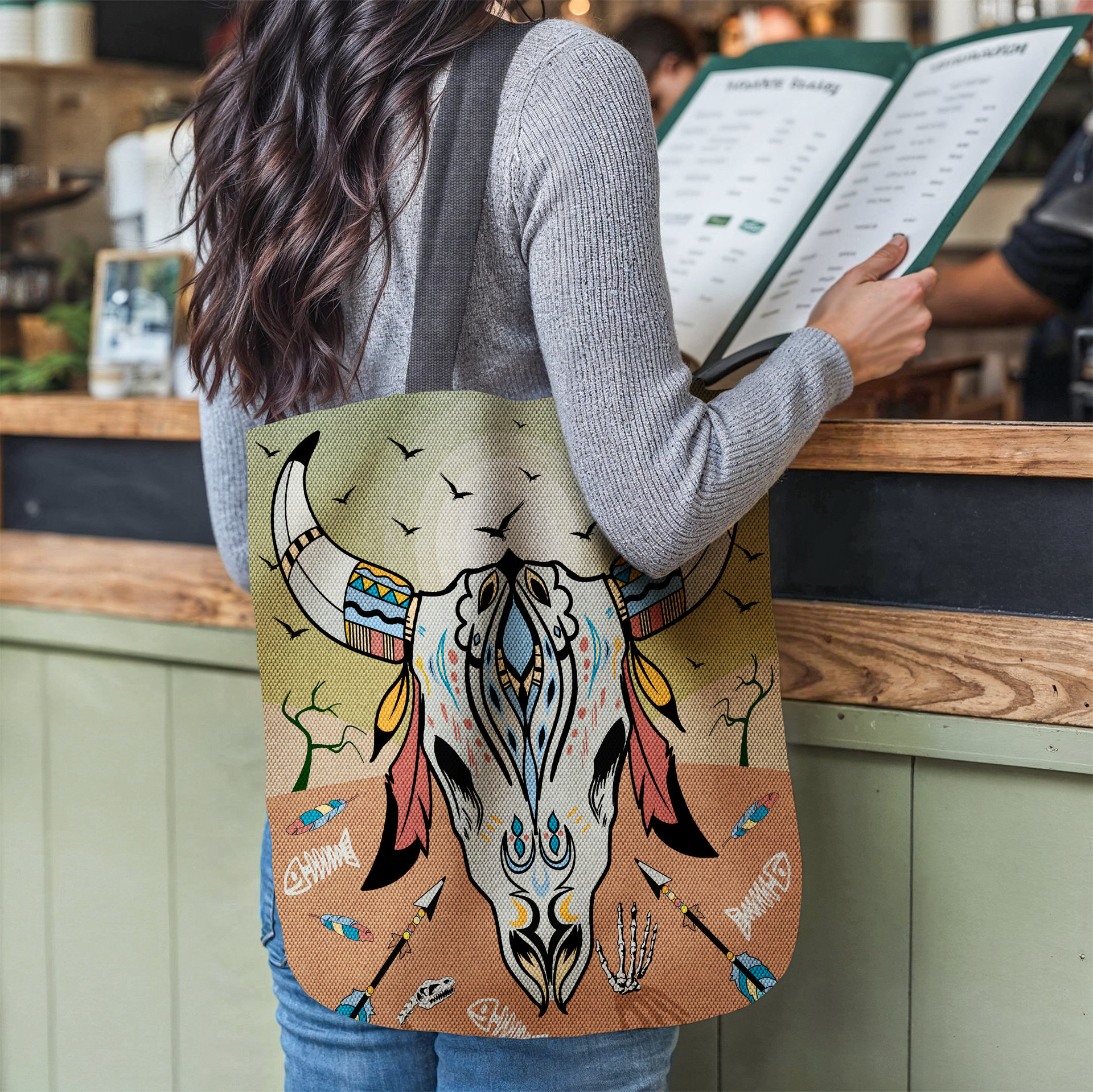 Cow Skull Tapestry Bag, Desert Sunset Colors tote hanging from the shoulder of a woman at a restaurant counter.