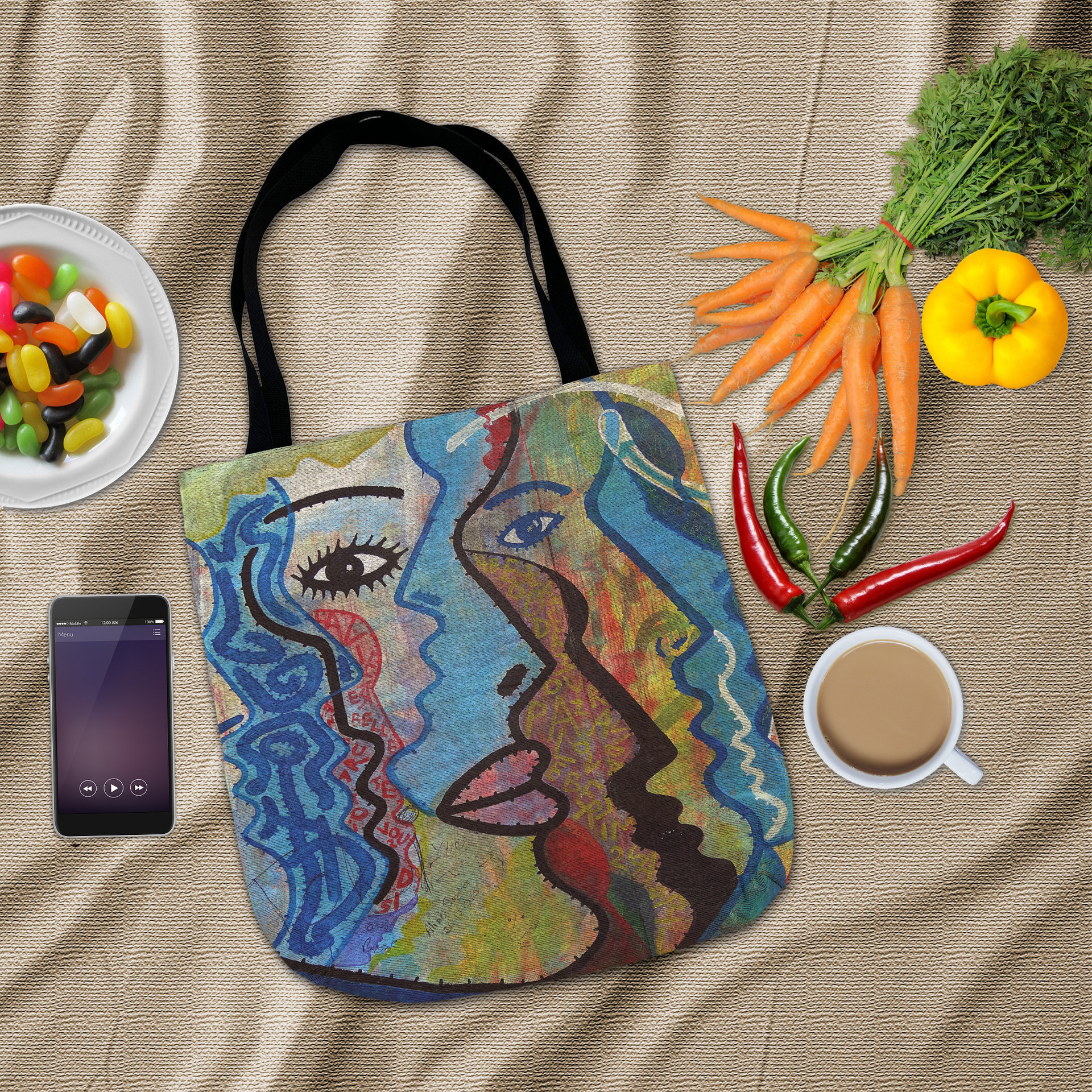 Flat lay Abstract Faces Woven Tote surrounded by vegetables, a bowl of jelly beans and a mobile phone.