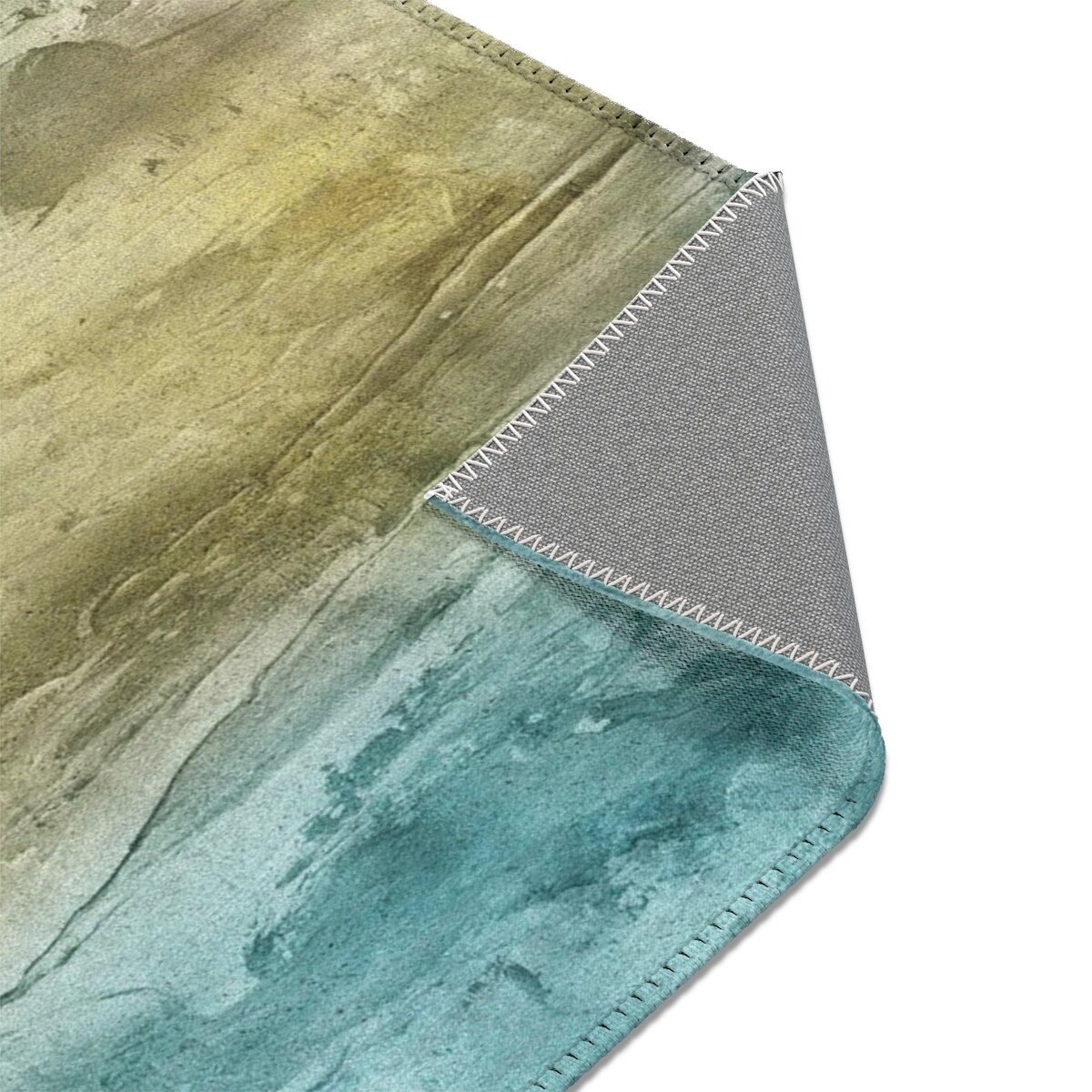Abstract watercolor rug in teal, sand, and olive tones, displaying the coated rug underside.