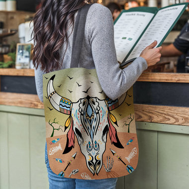 Cow Skull Tapestry Bag, Desert Sunset Colors tote hanging from the shoulder of a woman at a restaurant counter.