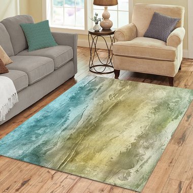Abstract watercolor rug in teal, sand, and olive tones, displayed in a cozy living room with wood floors and neutral furniture.